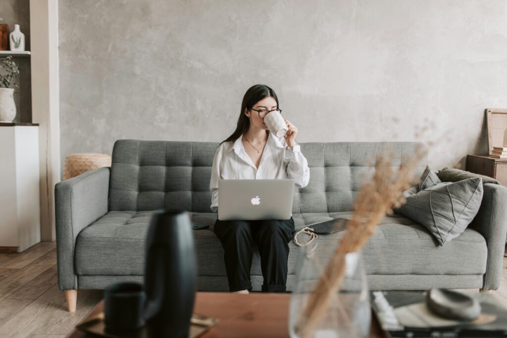 pexels-photo-4050289-4050289 Woman sipping coffee while working on a laptop in a cozy home setting, highlighting remote work lifestyle.