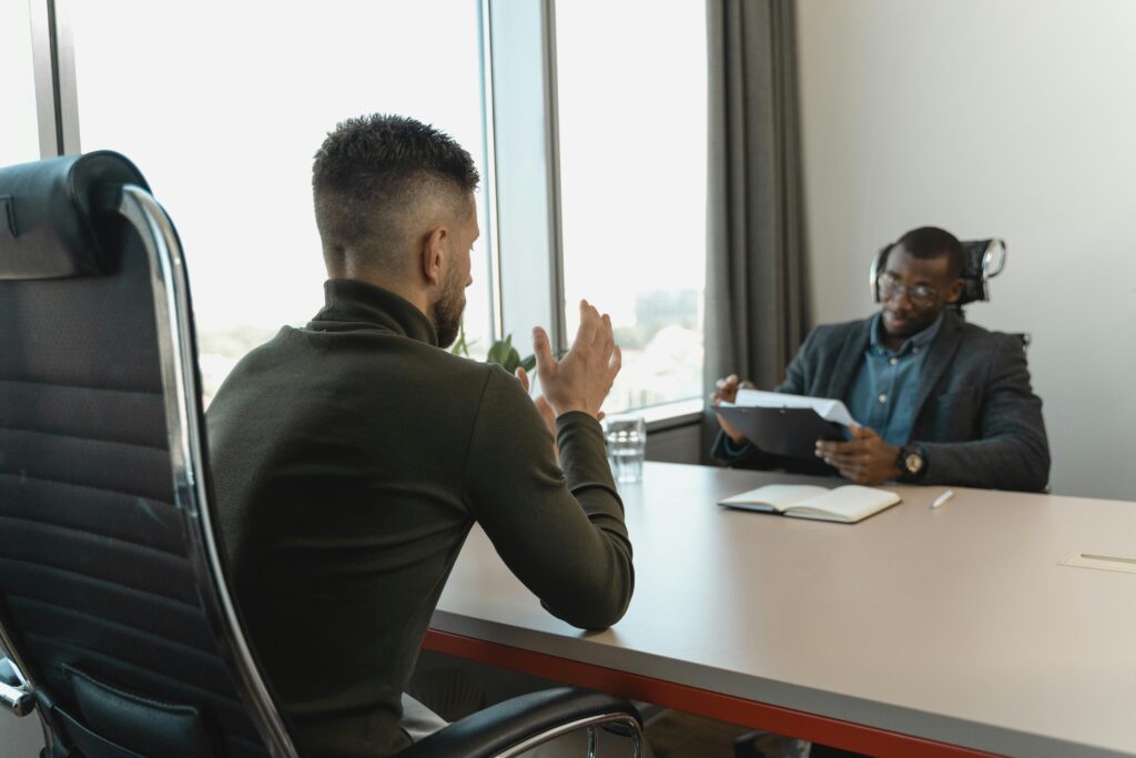 pexels-photo-5439368-5439368 Two men in a job interview setting in a modern office with large windows.