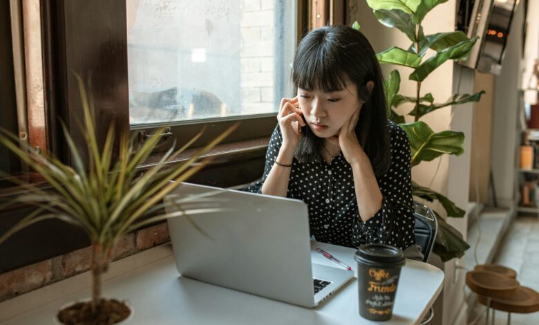 Asian woman focused on work in a modern office setting with laptop and coffee.