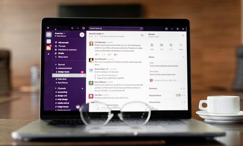 Laptop displaying a messaging app, with eyeglasses and coffee cup on a wooden table.